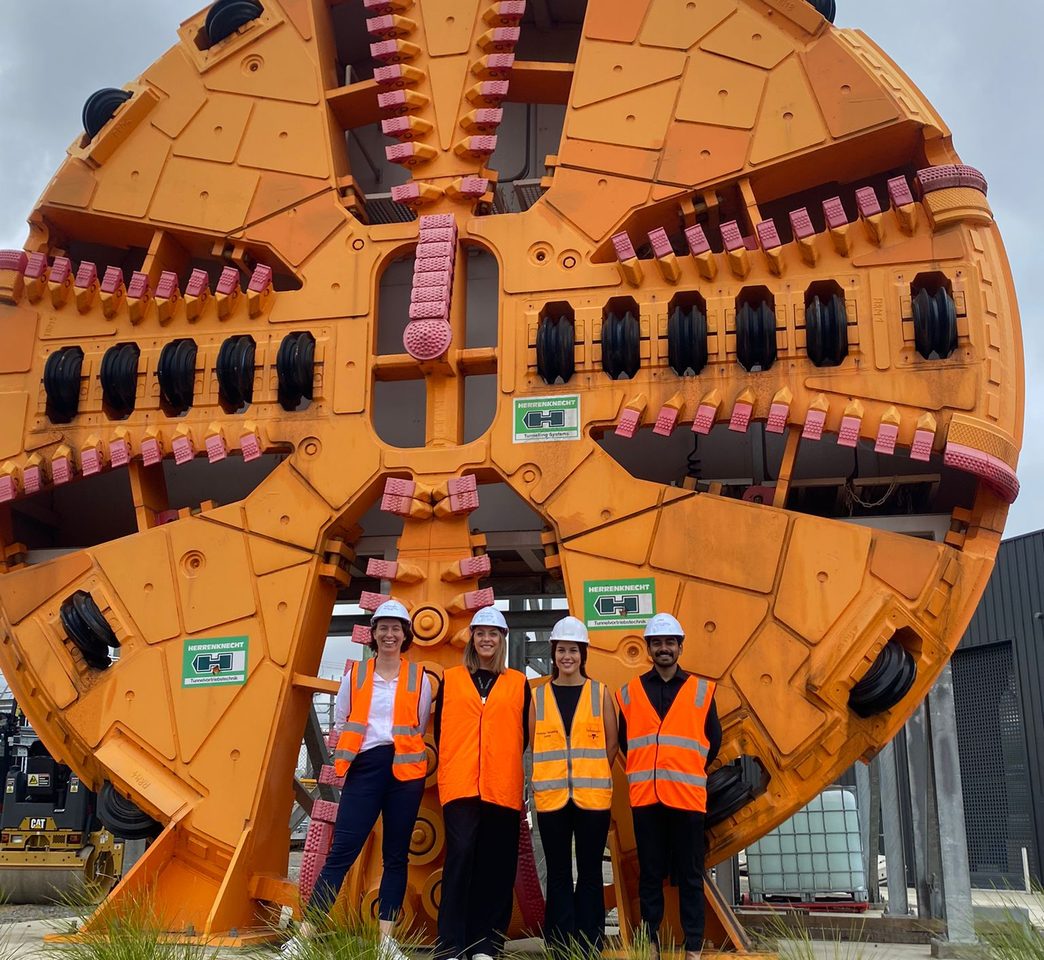 The iottag team in hard hats and hi-vis vests standing in front of a tunnel boring machine cutterhead