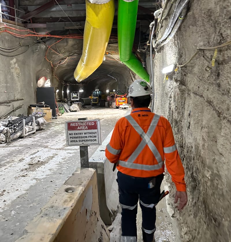 Worker walking past a restricted area sign in a tunnel lined with ventilation ducting