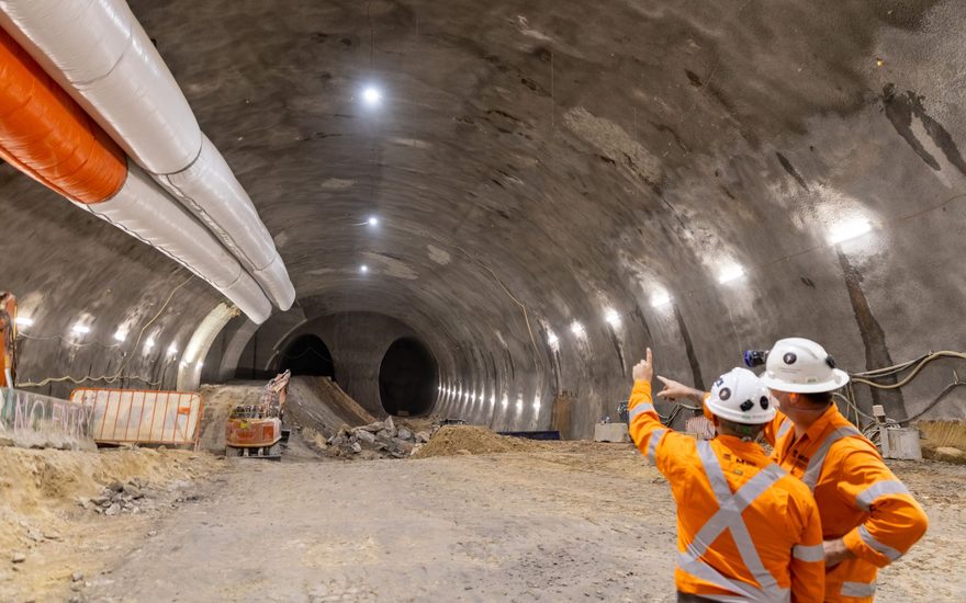Two workers in high-visibility orange inspecting a large excavated tunnel cavern
