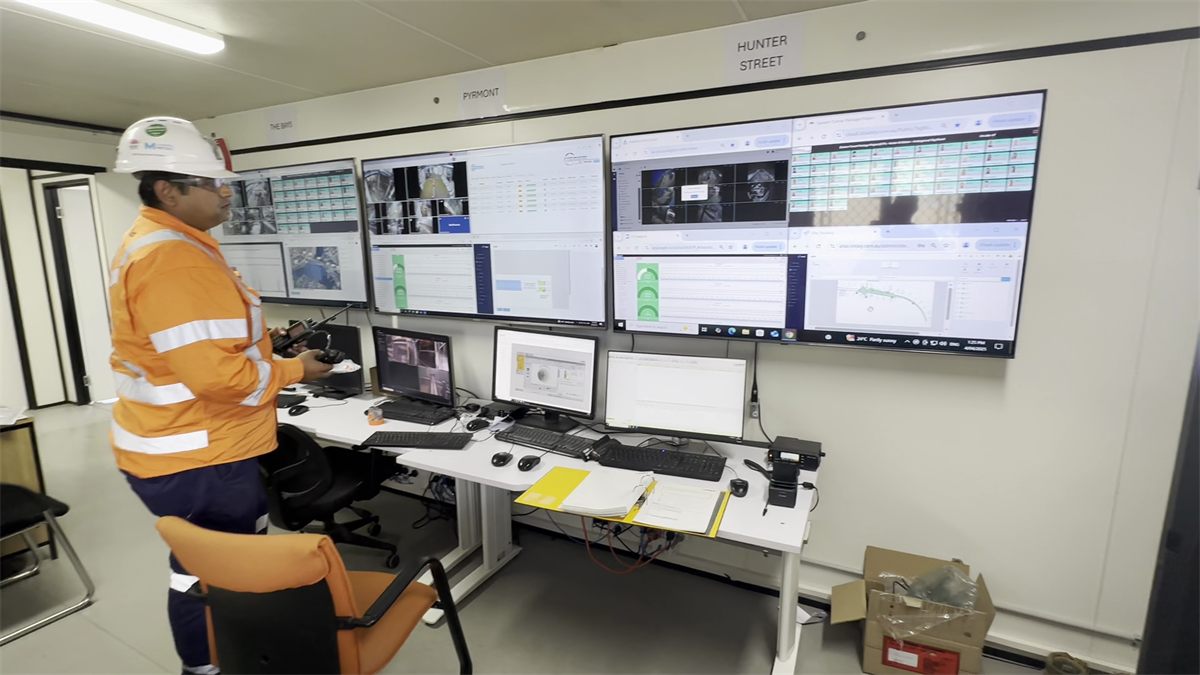 Operator in a site control room monitoring banks of live screens showing environmental and production data