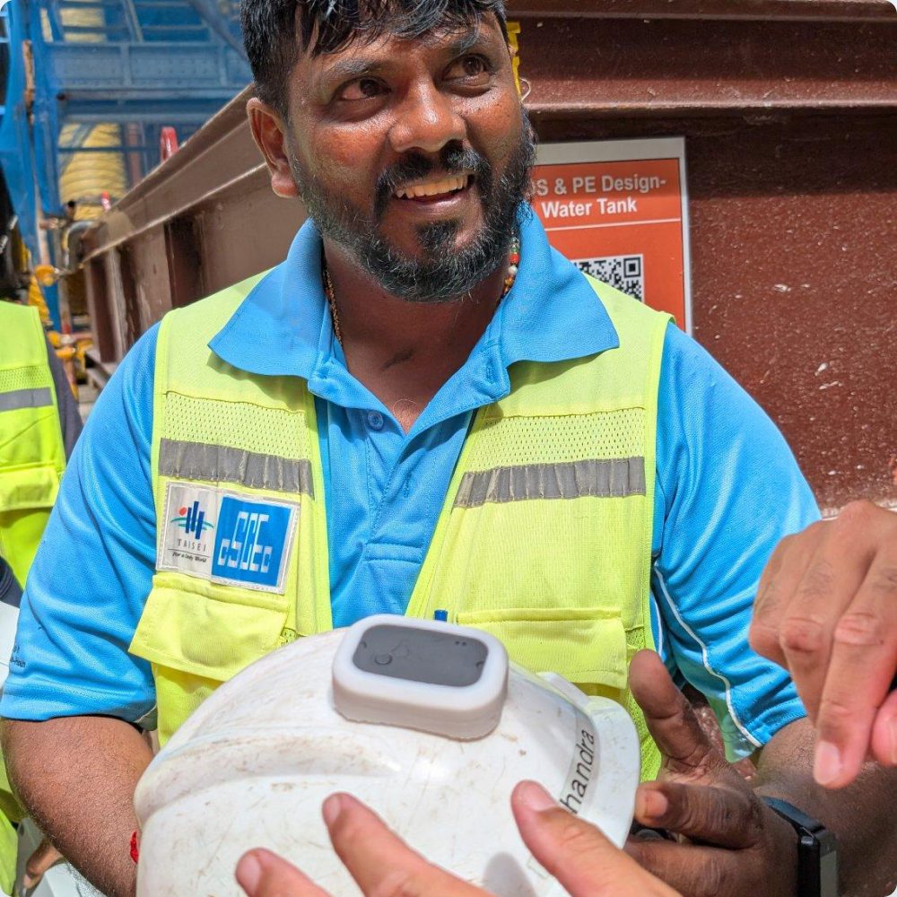 Worker in a high-visibility vest holding a helmet fitted with an iottag Vector Wearable