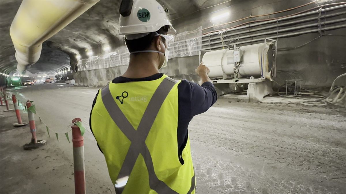 Worker in an iottag high-visibility vest inspecting a ventilation fan in an underground tunnel