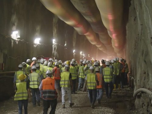 Workers in high-visibility clothing walking through an underground tunnel