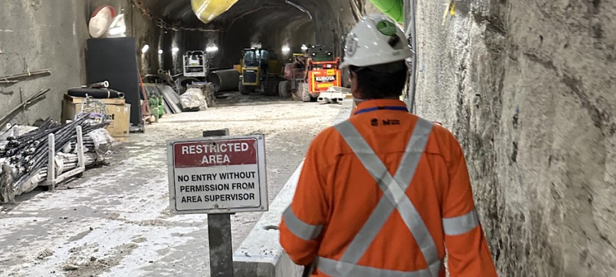 Worker passing a restricted area sign in a ventilated underground tunnel