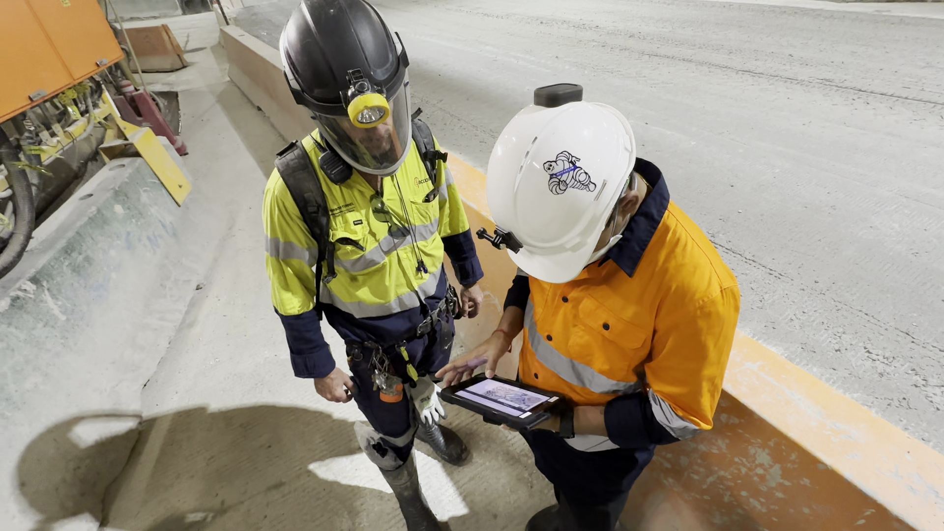 Two workers reviewing live operational data on a tablet beside a tunnel roadway