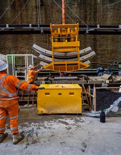Machinery lifting tunnel lining segments beside a worker